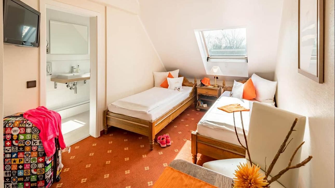 Cozy attic bedroom with twin beds, white walls, skylight, and bright orange accents