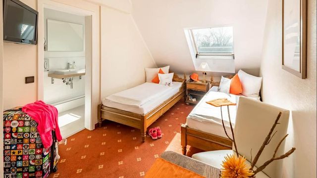 Cozy attic bedroom with twin beds, white walls, skylight, and bright orange accents