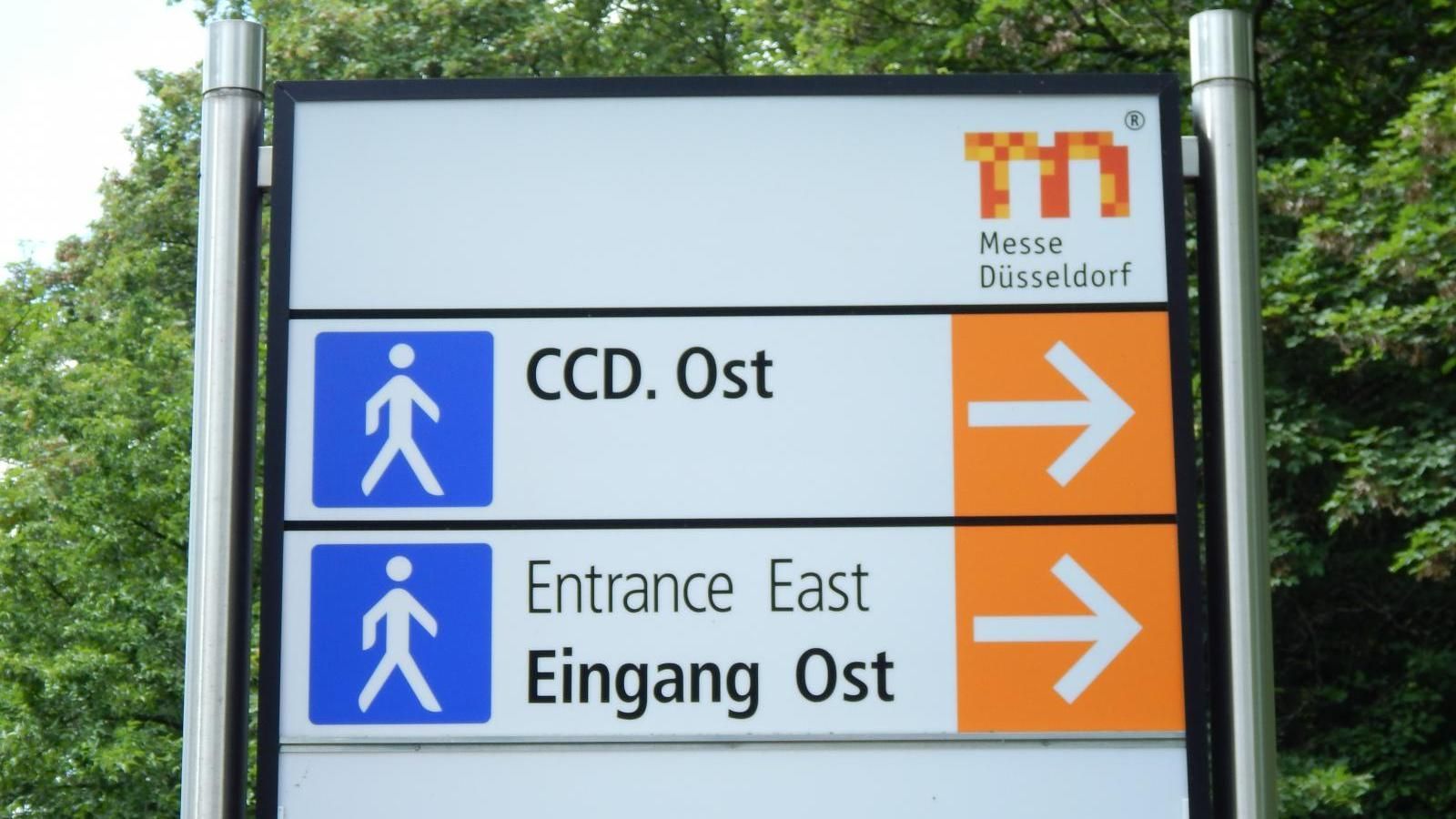 Blue and orange directional signs for accessible entry, labeled “CCD. Ost” and “Eingang Ost” with right arrows.