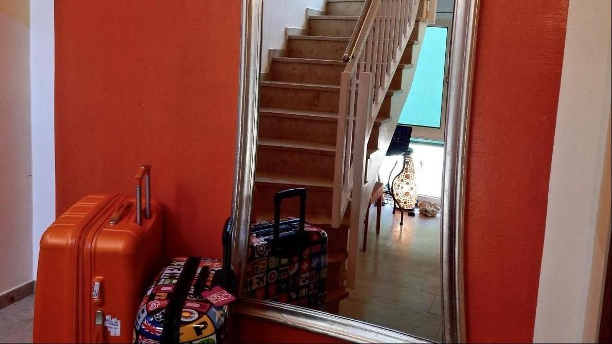 Hallway with red walls, staircase, mirror, and stacked orange suitcases near the door
