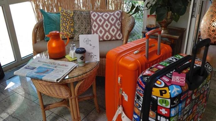 Patio seating area with wicker chairs, orange decor, and a colorful suitcase beside a small table