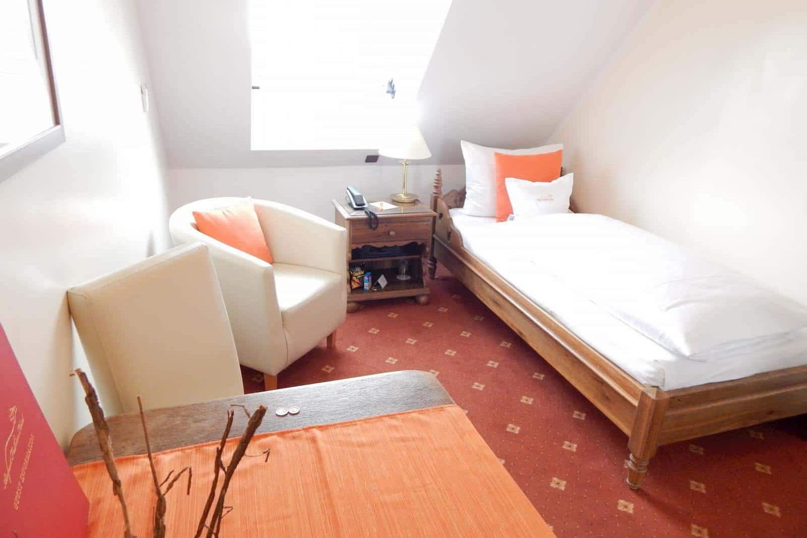 Bright bedroom with twin bed, white armchair, and orange rug by sunlit window