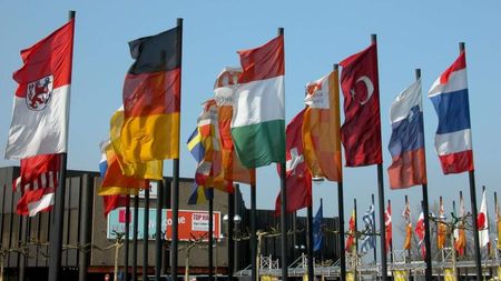 Rows of national flags on poles waving against a blue sky at an outdoor event
