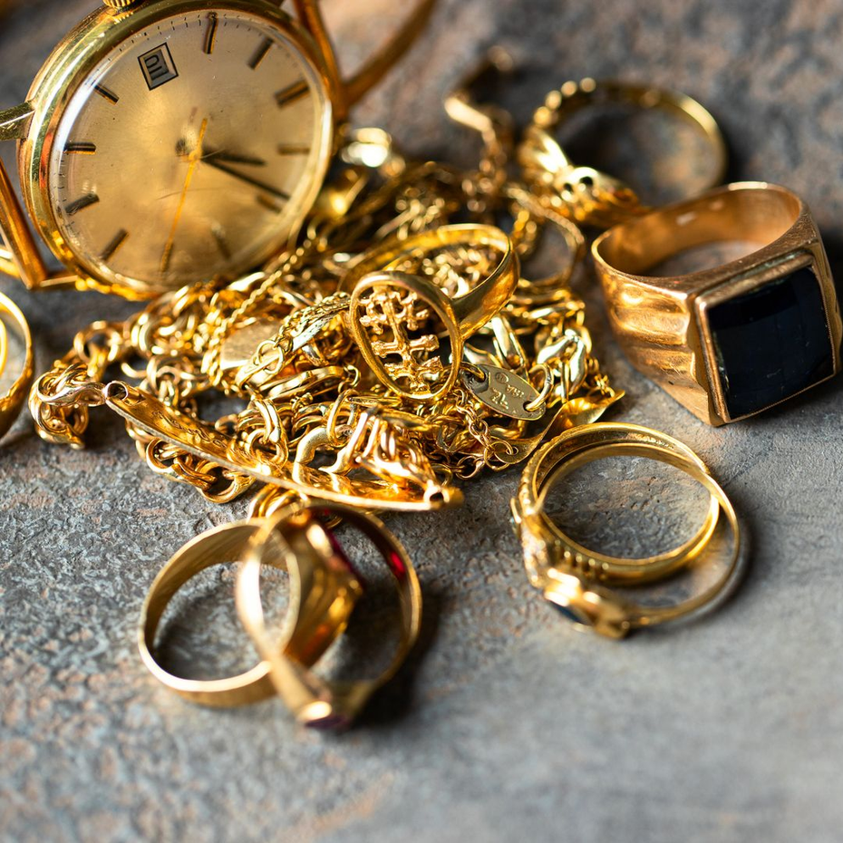 Bijoux en or : montre, bagues et chaîne sur une surface texturée.