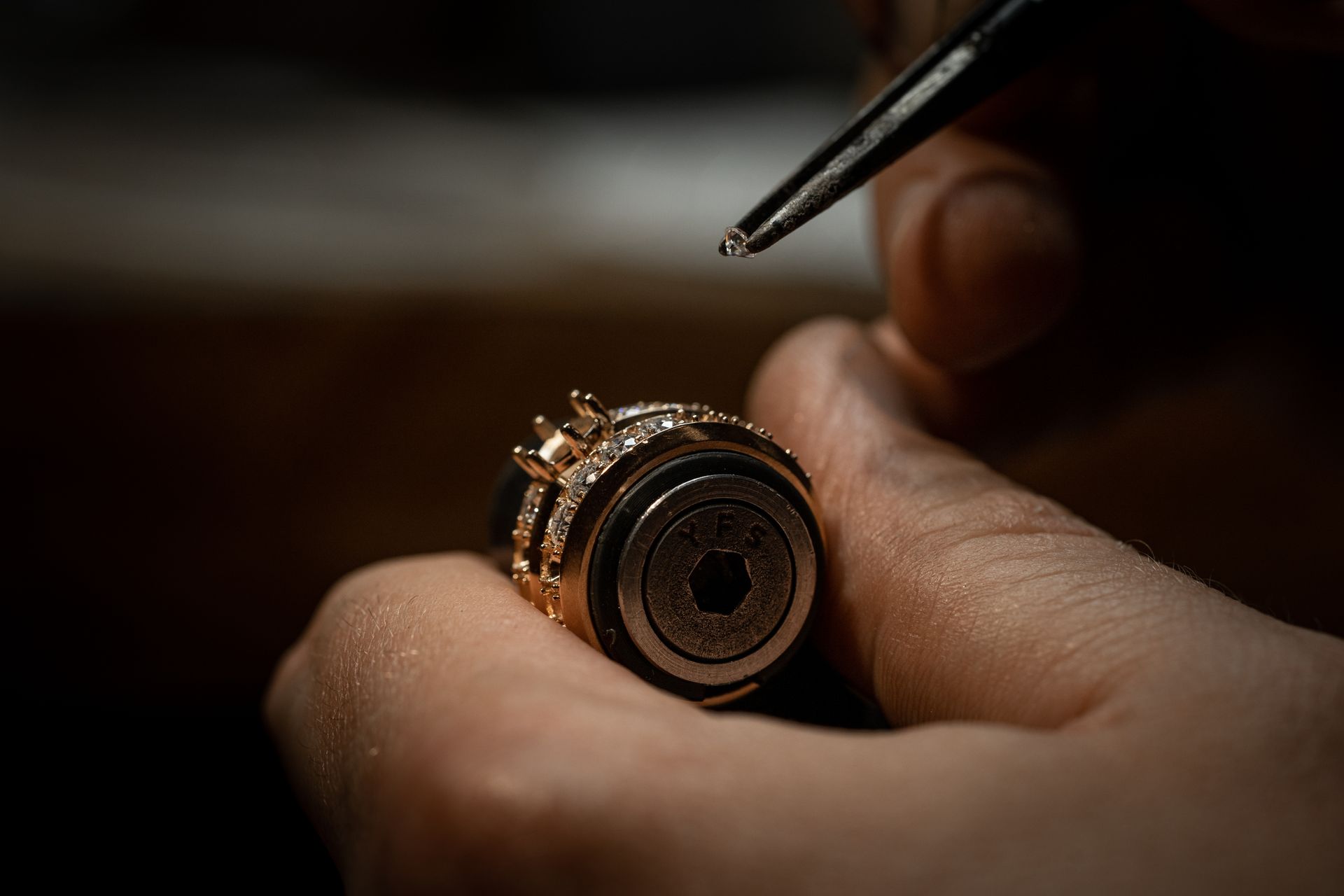 Un bijoutier utilise une pince à épiler pour sertir une petite pierre précieuse sur une bague en or maintenue dans un outil.