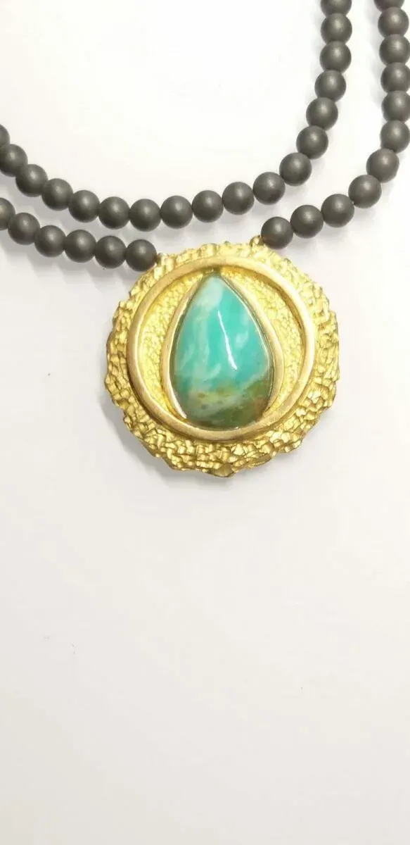 Un collier avec un pendentif turquoise serti d'or, sur un rang de perles foncées.
