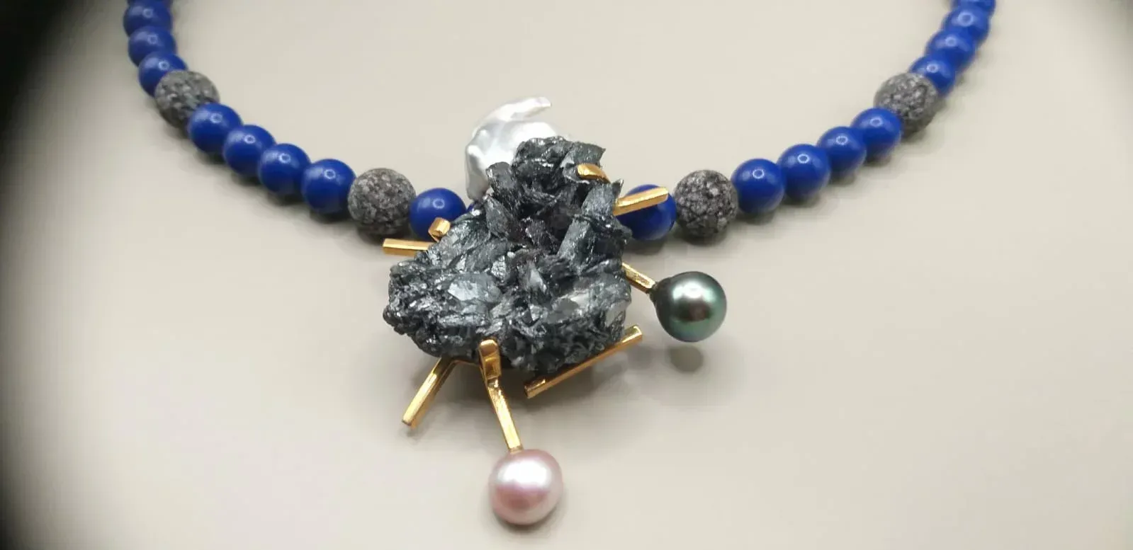 Collier de perles bleues avec un pendentif central en pierre grise, des accents dorés et deux perles.