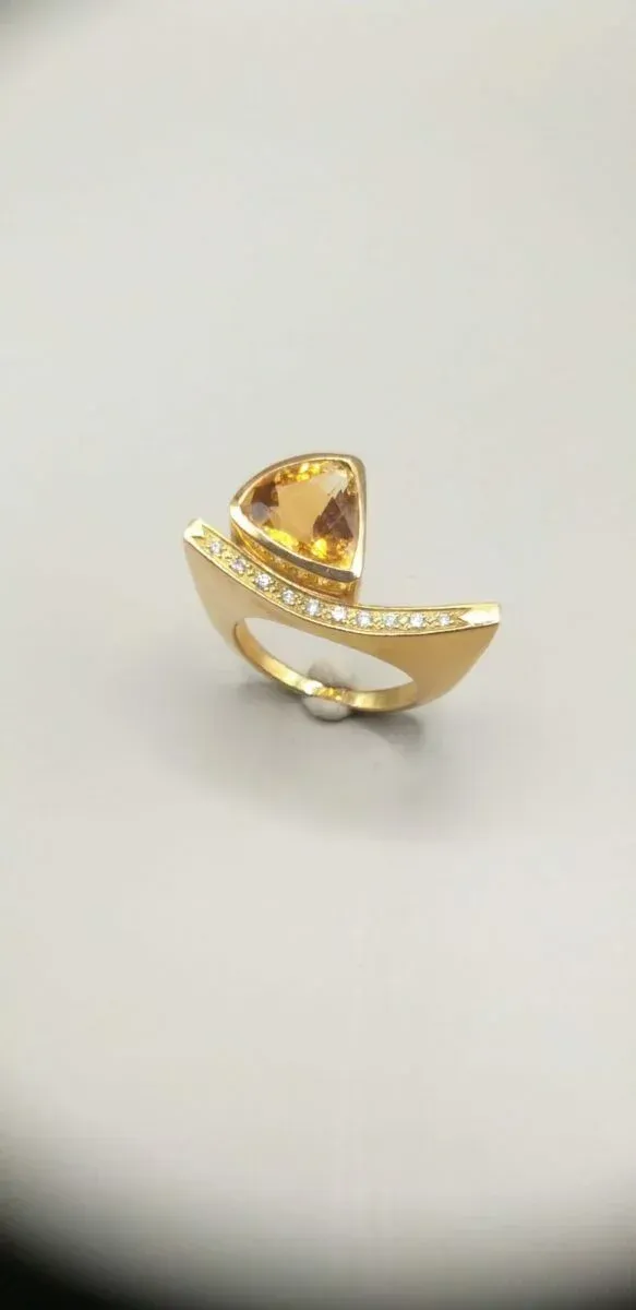 Bague en or avec une grosse pierre précieuse orange et de petits diamants, sur fond blanc.