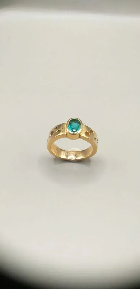 Bague en or avec pierre précieuse bleu sarcelle sur une surface blanche.