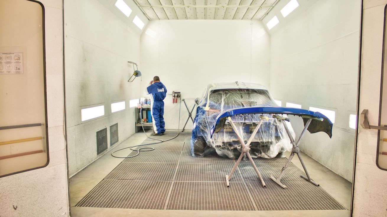 Un peintre automobile se préparant à repeindre le parechoc d'une voiture bleu dans l'atelier