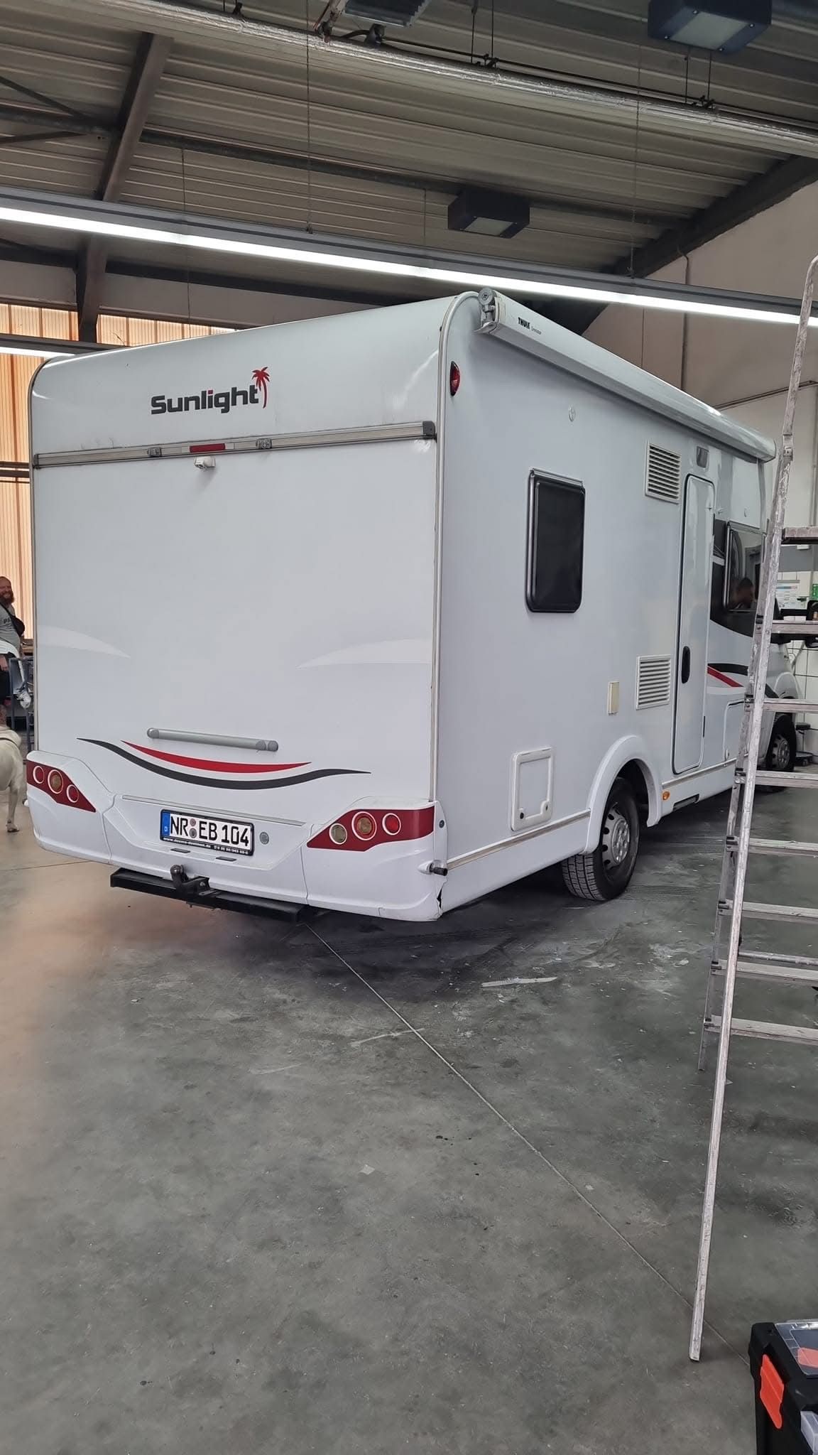 Ein weißes Wohnmobil steht in einer Garage neben einer Leiter.