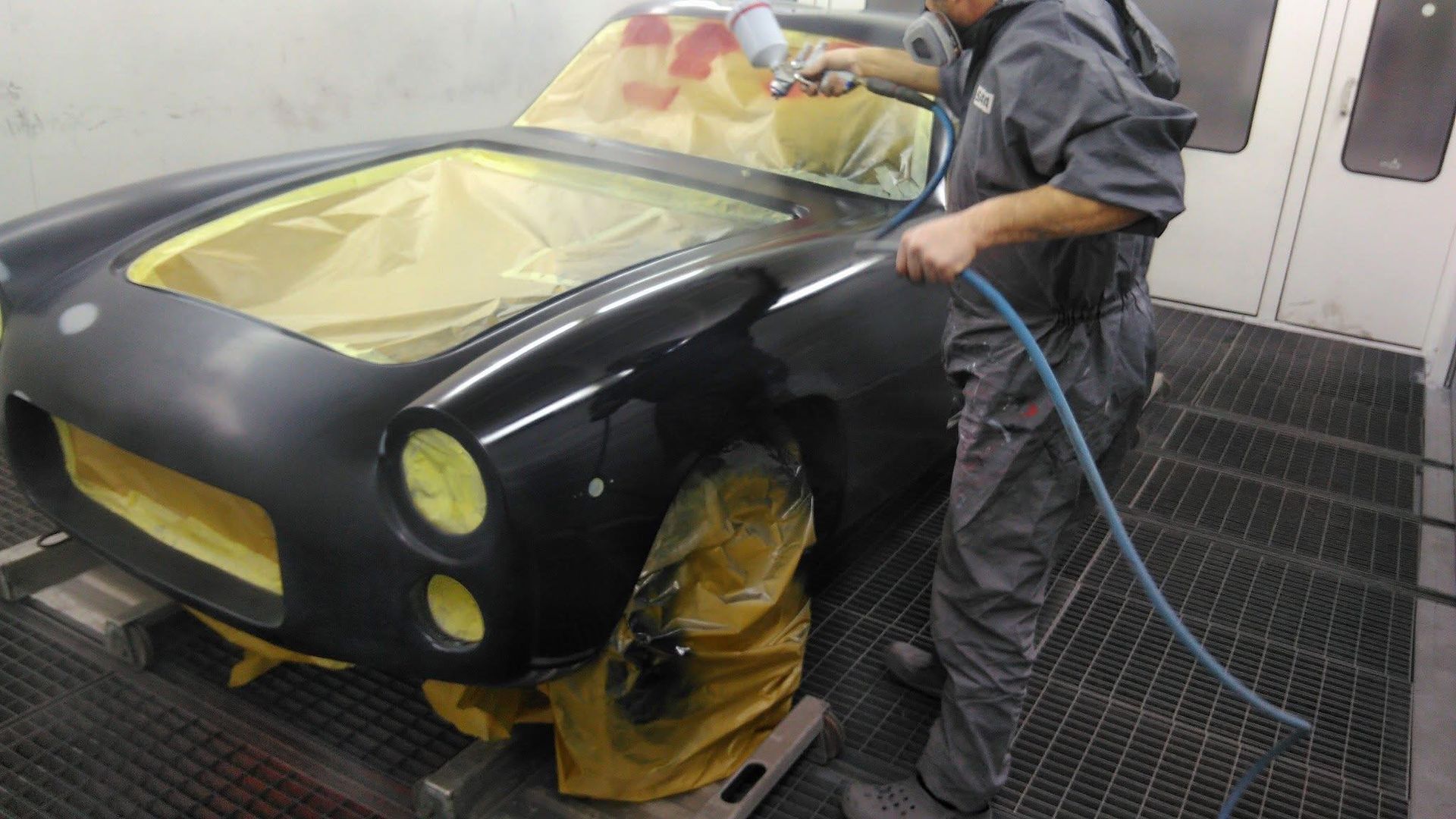 Ein Mann bemalt in einer Lackierkabine ein Auto mit Sprühfarbe.