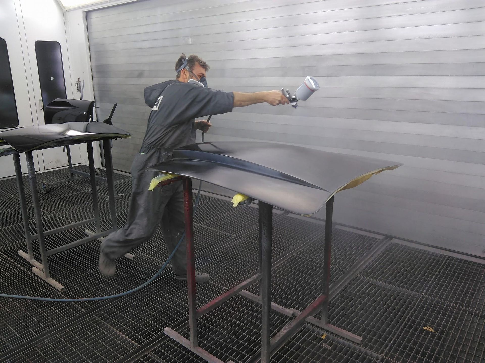 Ein Mann bemalt ein Auto in einer Lackierkabine mit Sprühfarbe