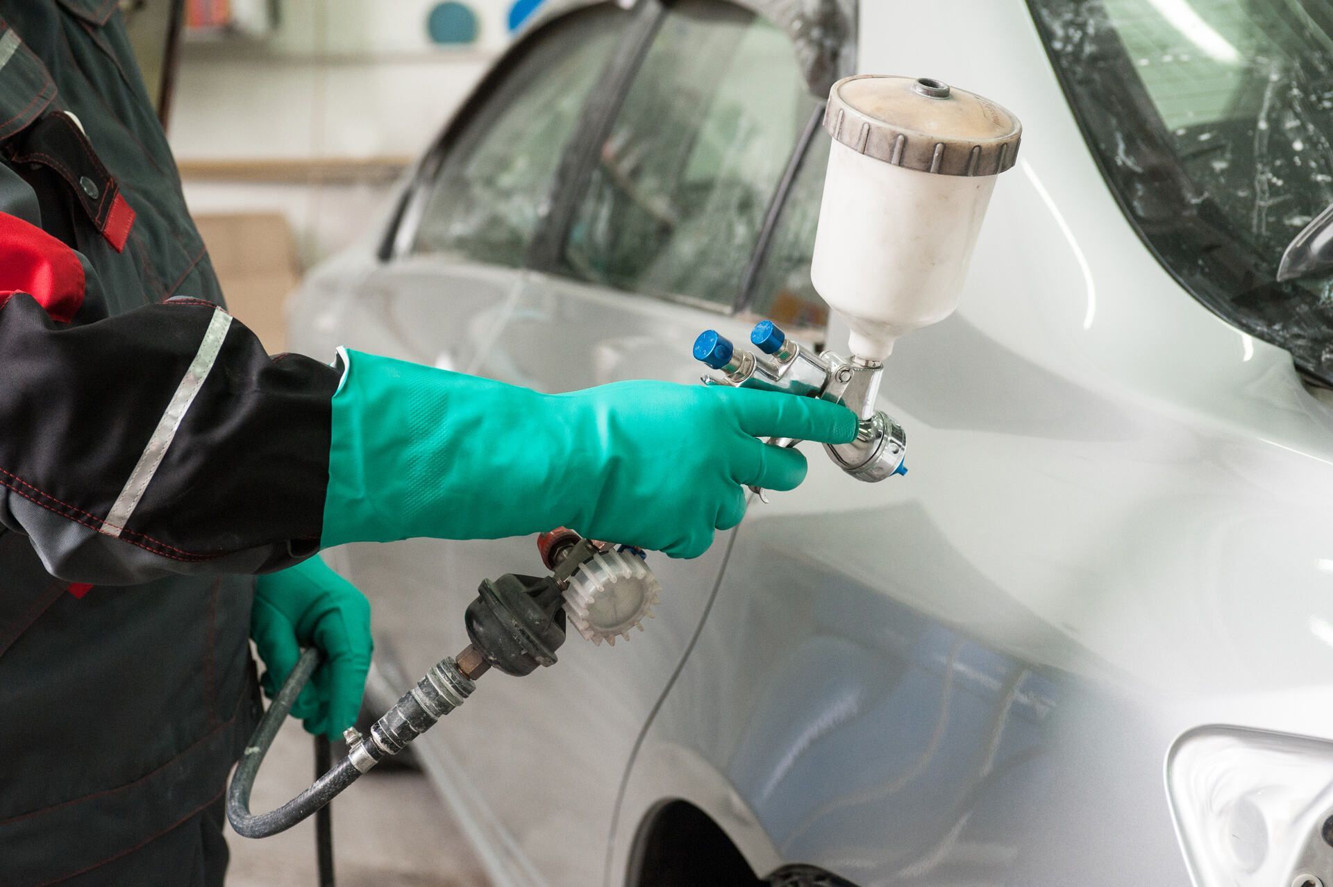 Ein Mann mit grünen Handschuhen sprüht Farbe auf ein Auto.