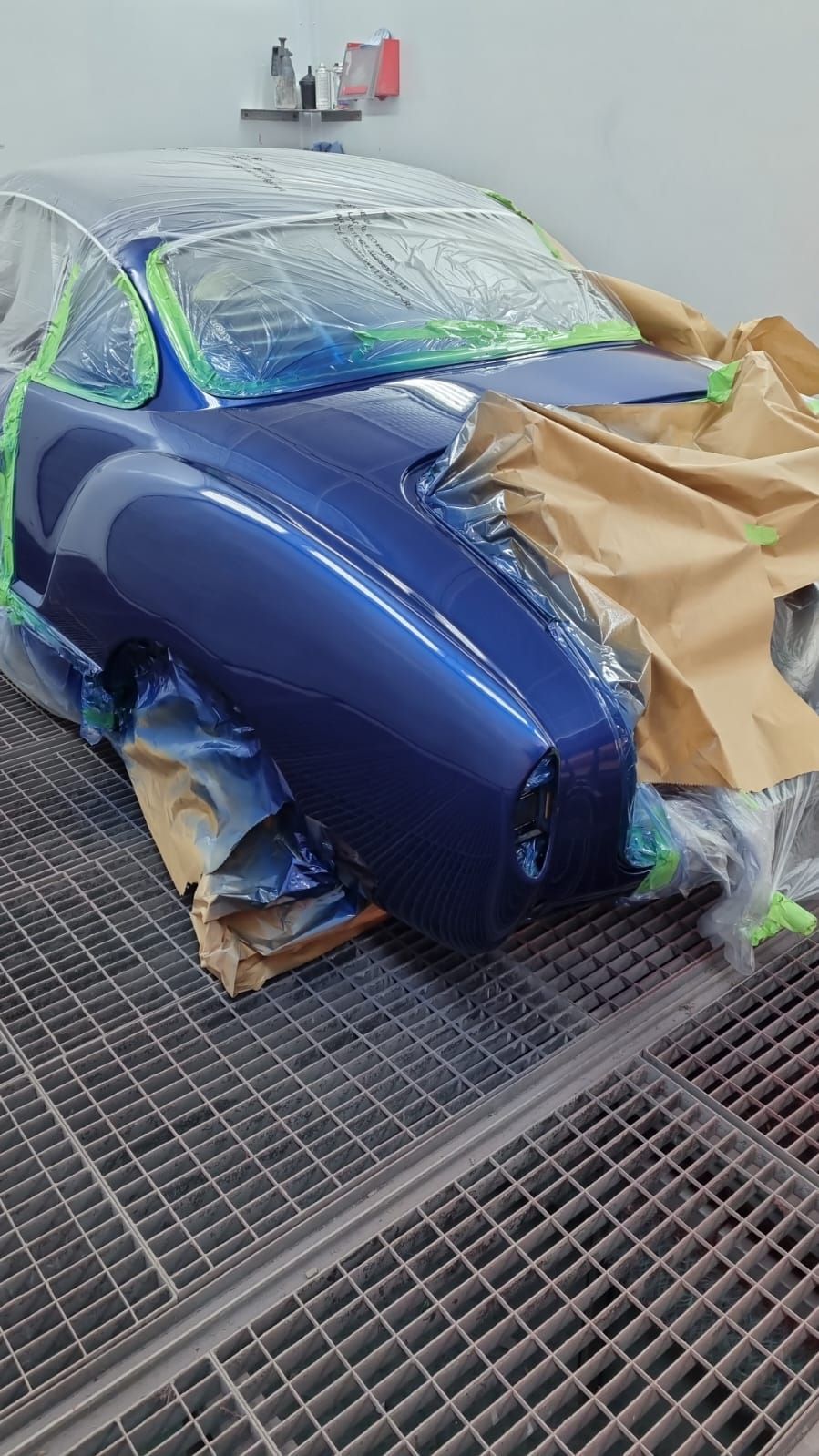 Ein blaues Auto wird in einer Lackierkabine lackiert.