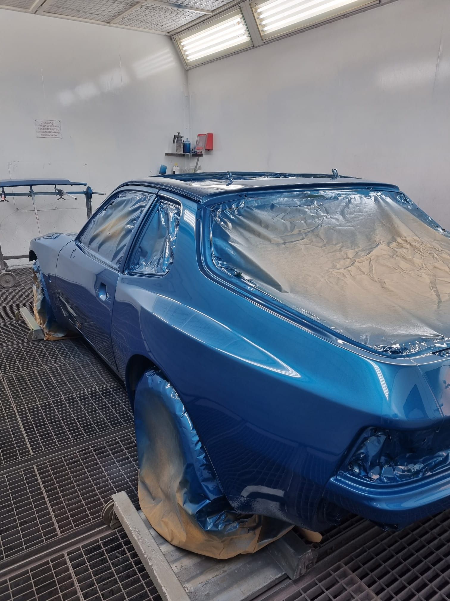 Ein blaues Auto steht in einer mit Plastik abgedeckten Lackierkabine.