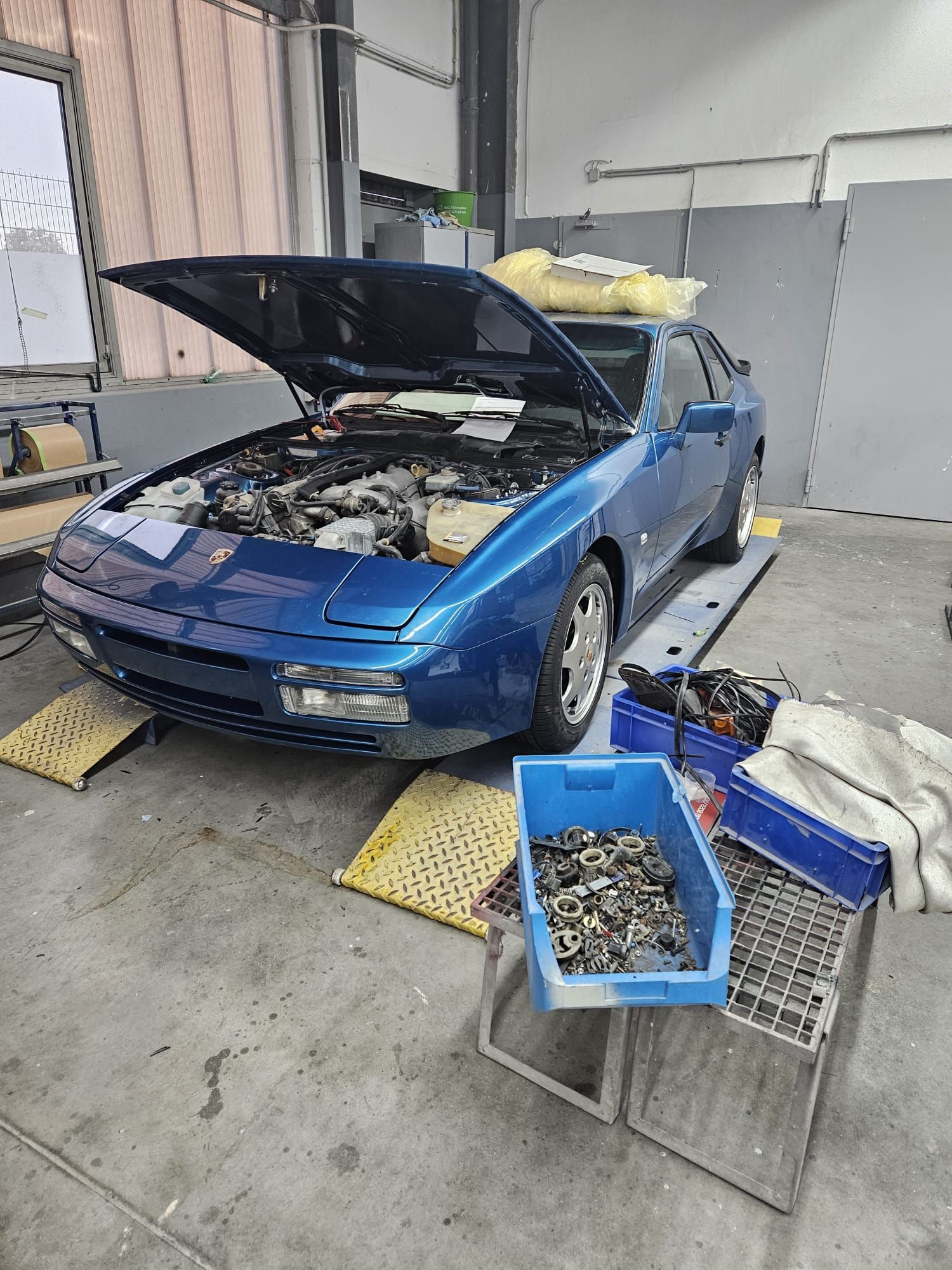 Ein blaues Auto mit geöffneter Motorhaube steht in einer Garage.