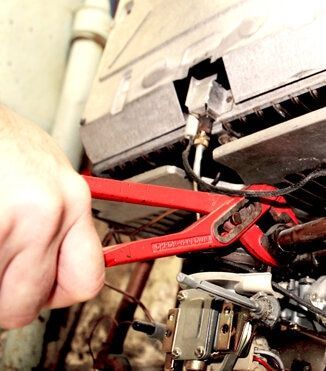 Une main utilise une pince réglable rouge pour serrer un tuyau métallique à l'intérieur d'un appareil.