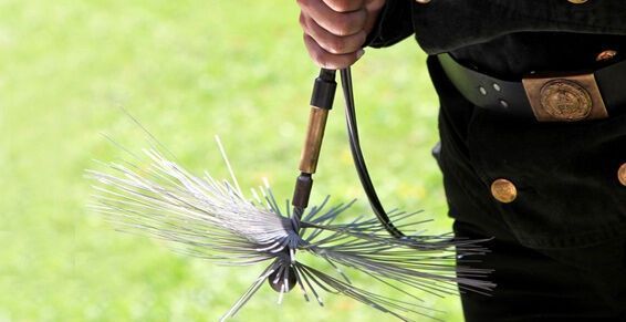Un ramoneur en uniforme noir tenant une brosse métallique pour le nettoyage des conduits de cheminée.