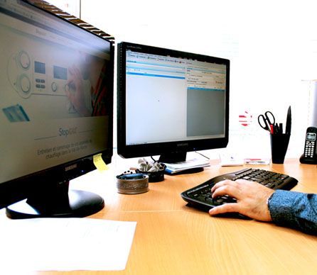 Une personne tapant sur un clavier d'ordinateur à un bureau équipé de deux écrans et de fournitures de bureau.