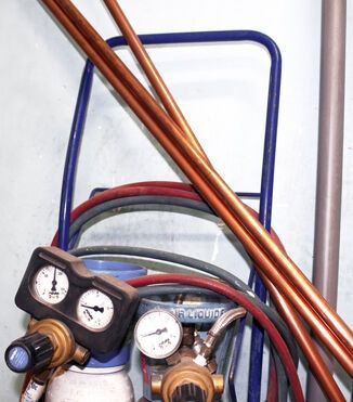Un chariot pour bouteilles de gaz avec manomètres et tuyaux de soudage, avec des tuyaux en cuivre appuyés sur le châssis.