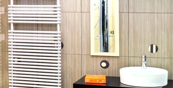 Une salle de bains moderne comprend un sèche-serviettes blanc, un lavabo vasque sur un meuble-lavabo foncé et un miroir rectangulaire sur un mur en bois.