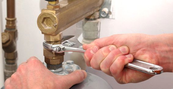Des mains utilisent une clé réglable pour serrer un raccord en laiton sur un tuyau relié à un réservoir.