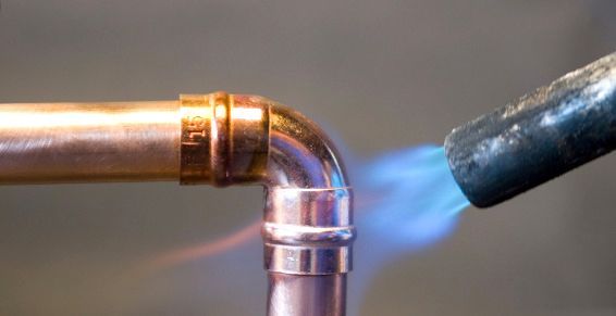 Une torche portative utilise une flamme bleue pour souder un raccord de tuyau en cuivre.