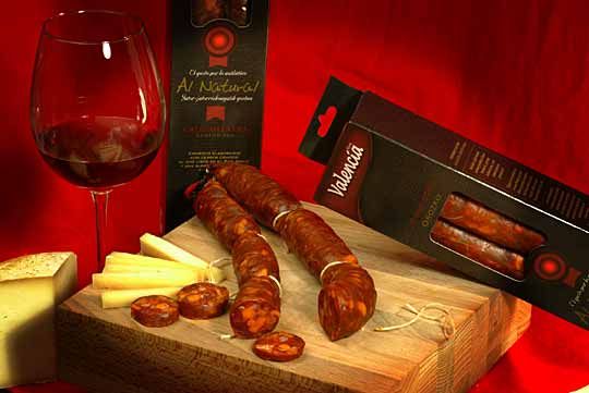 Una caja de salchichas valencianas reposa sobre una tabla de cortar de madera al lado de una copa de vino.