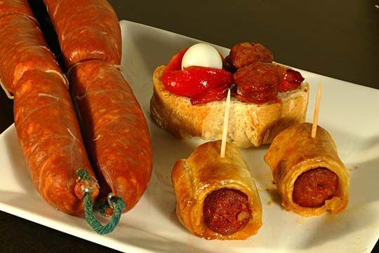 Un plato blanco cubierto con rollitos de salchicha y un sándwich.