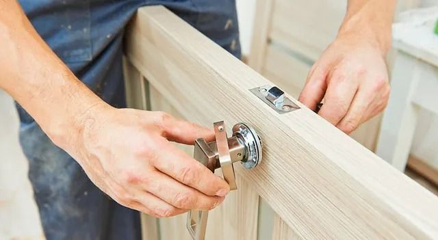 Un hombre está instalando un pomo en una puerta de madera.
