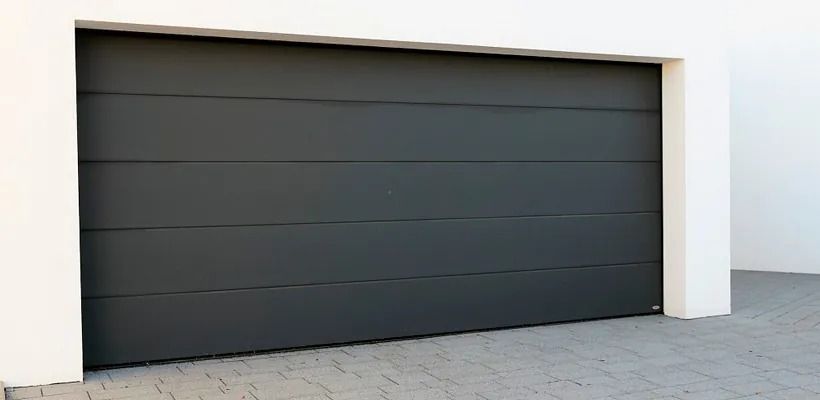 Una puerta de garaje negra está delante de un edificio blanco.