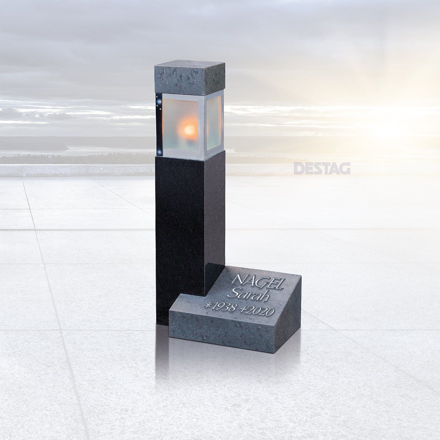 Grabstein mit rechteckigem Sockel aus schwarzem Granit und einer Spitze, in der ein leuchtendes Licht ruht. Graues, abgewinkeltes Stück mit eingraviertem Namen.