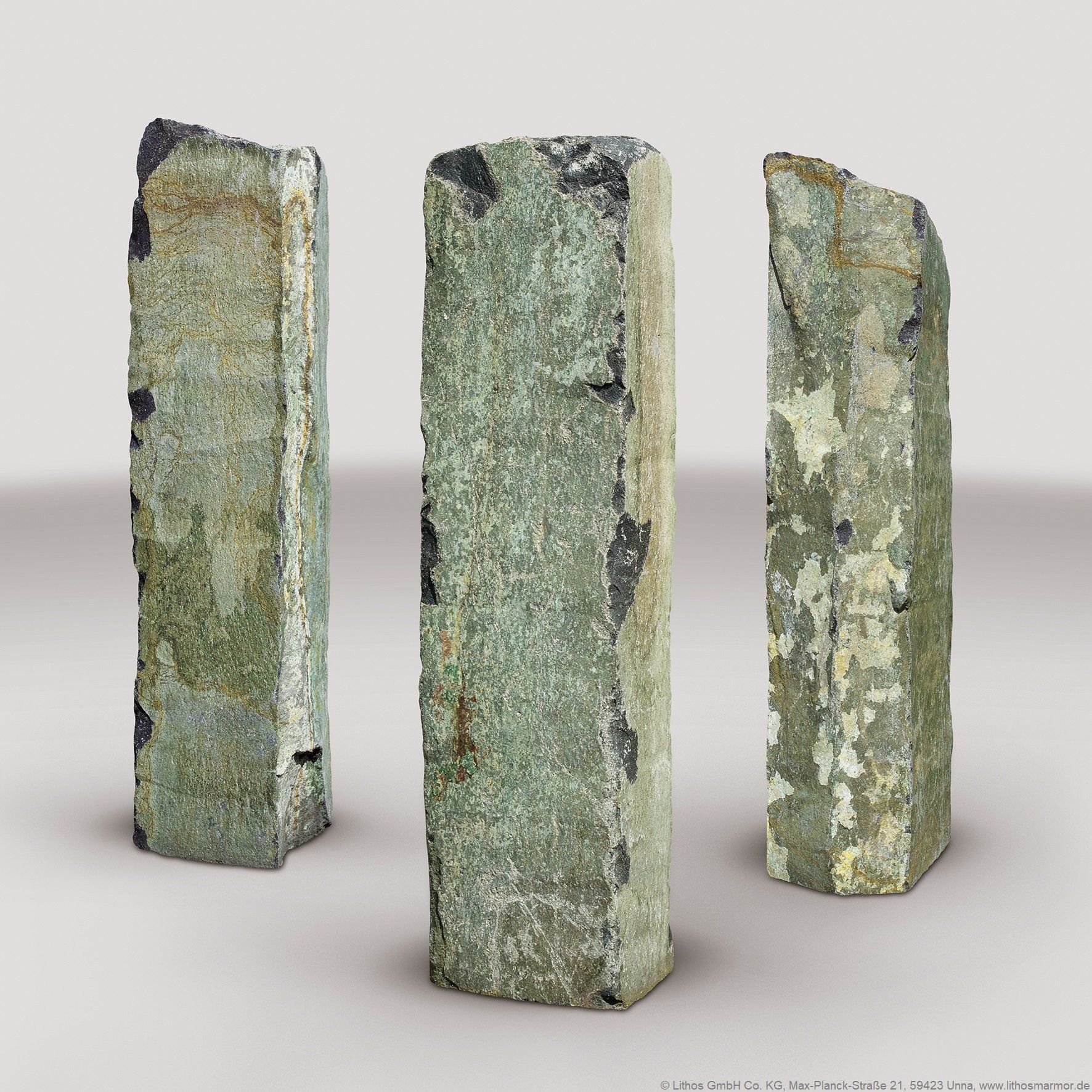 Drei verwitterte, rechteckige Steinsäulen mit fleckiger grüner und grauer Färbung vor hellem Hintergrund.