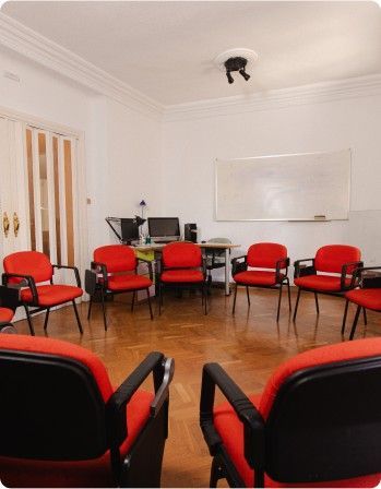 Sala de reuniones pequeña con sillas rojas dispuestas en círculo y una pizarra en la pared.
