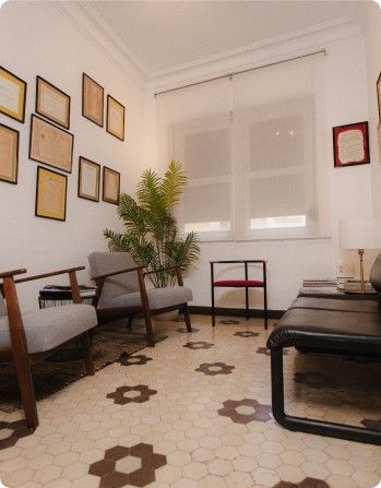Salón minimalista con sofás negros, cuadros enmarcados, una planta y suelo de baldosas estampadas