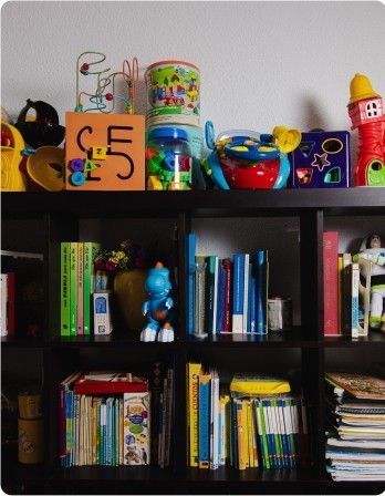 Estantería negra llena de libros de colores, con juguetes encima, frente a una pared clara.