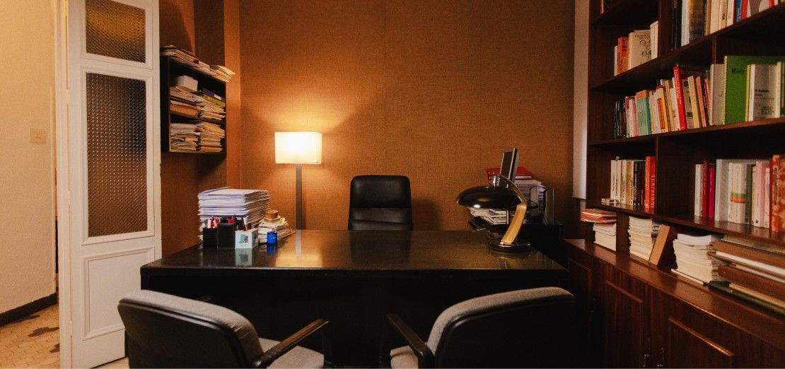 Acogedora oficina en casa con escritorio, silla, lámpara, estanterías y una computadora bajo una cálida iluminación