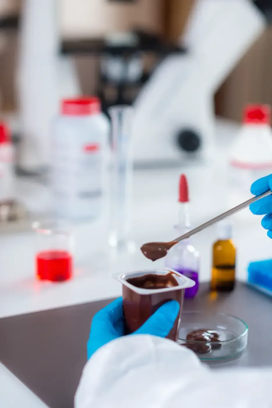 Behandschuhte Hände handhaben eine Probe in einem Labor, mit einer Pipette und Fläschchen auf einer weißen Werkbank.