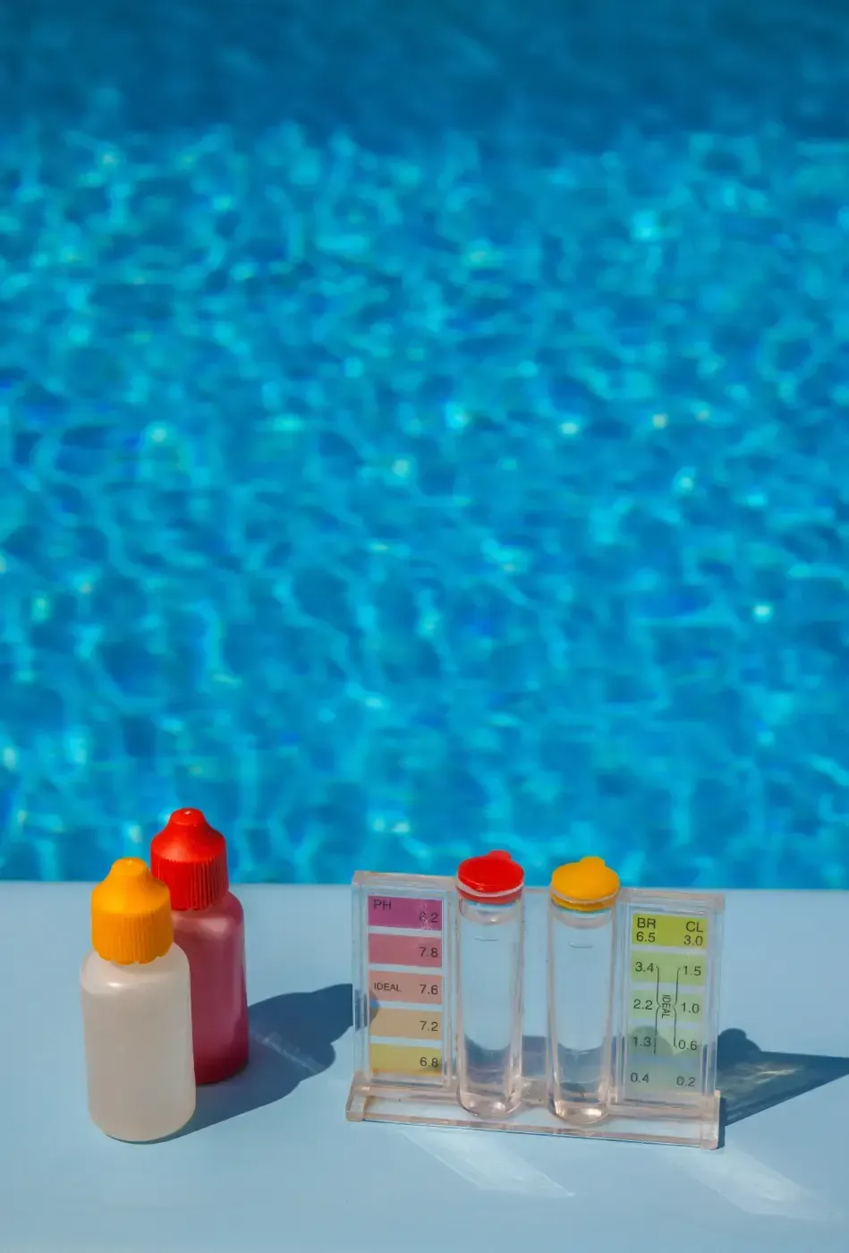 Schwimmteströhrchen und kleine Fläschchen auf einem Tisch am Pool neben blauem Wasser