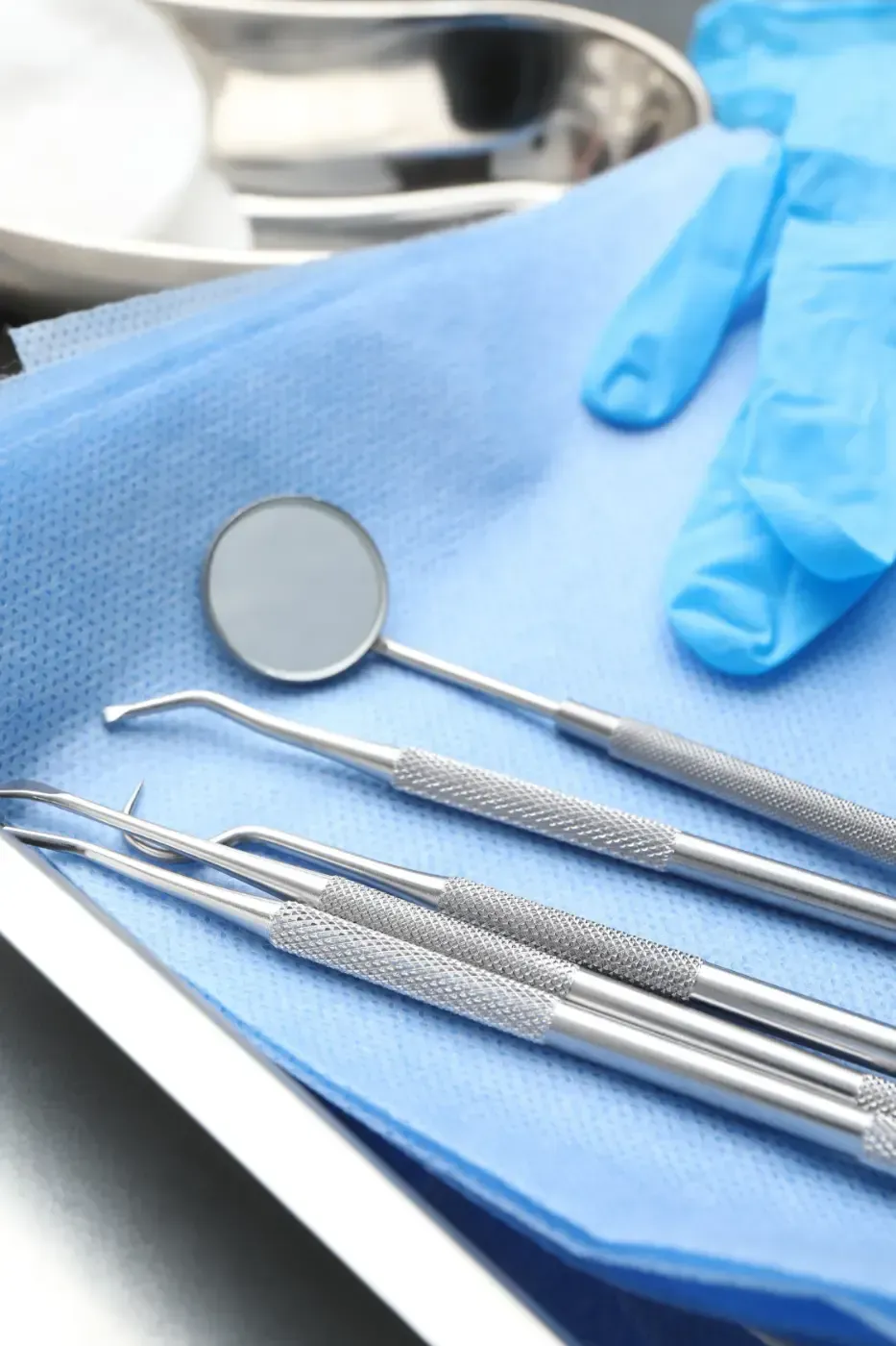 Zahnärztliche Instrumente, darunter ein Spiegel und Sonden, auf einem blauen Tuch neben einem Waschbecken.