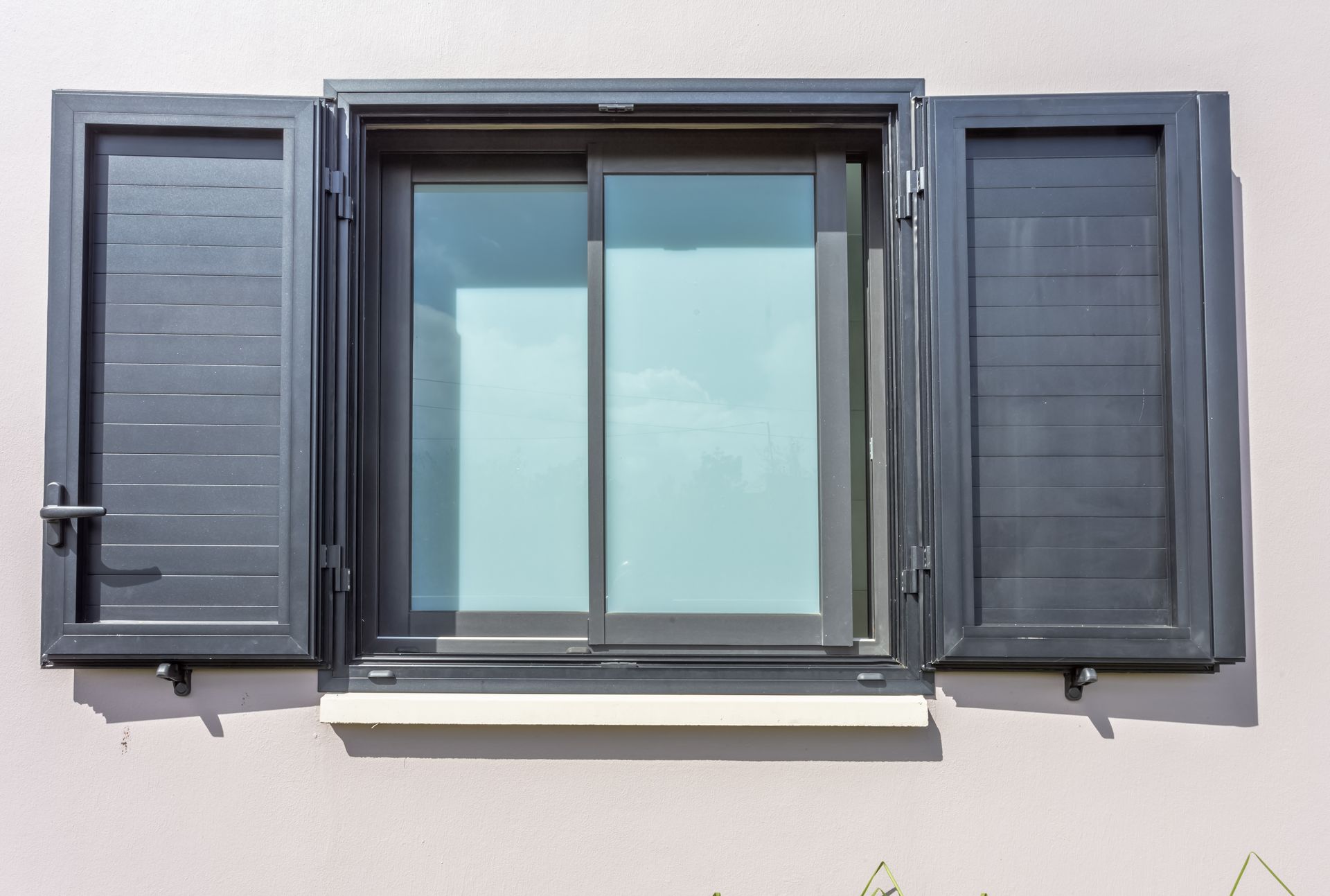 Fenêtre gris foncé aux volets ouverts sur un mur rose clair.