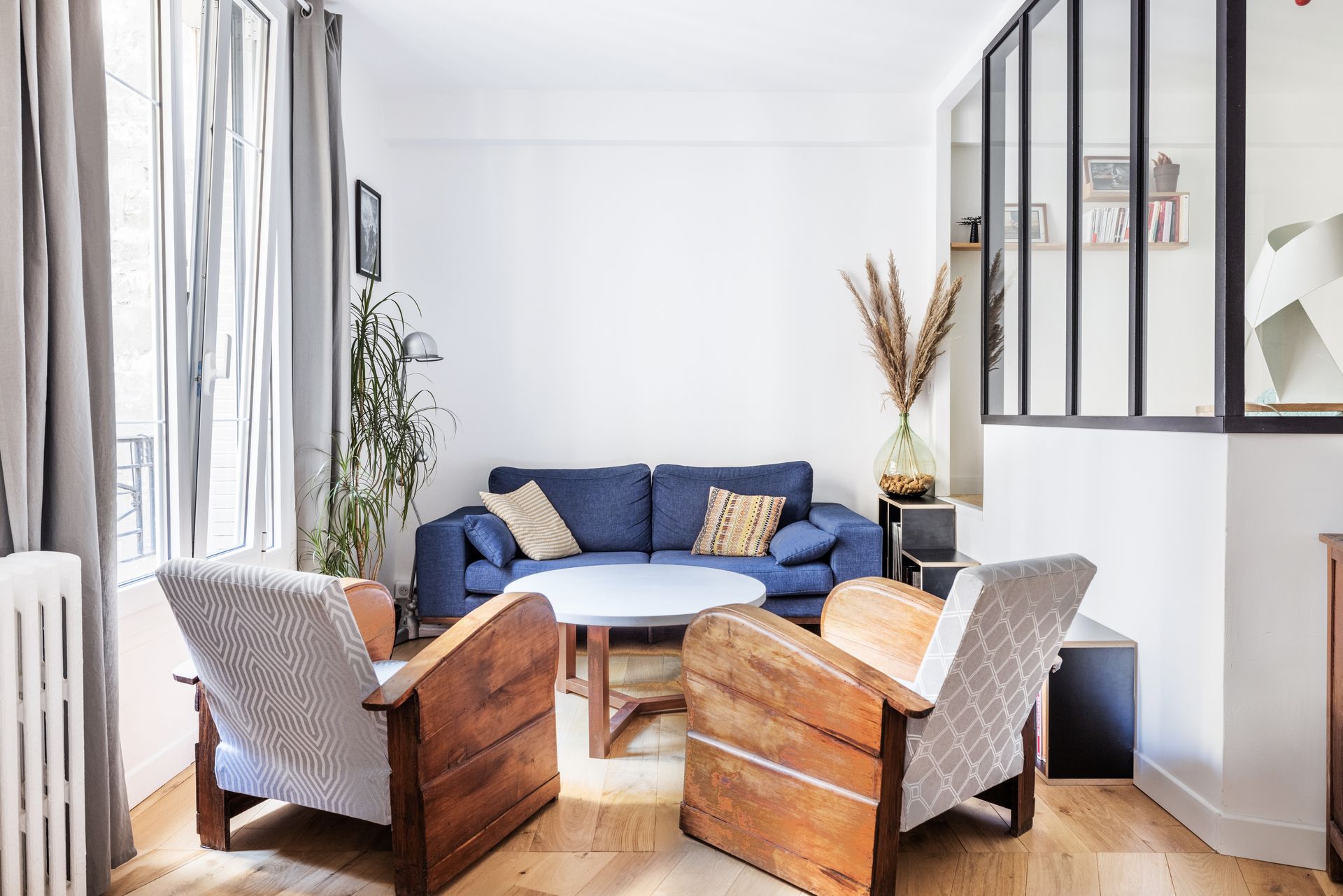 Salon avec canapé bleu, chaises en bois et table basse ronde.