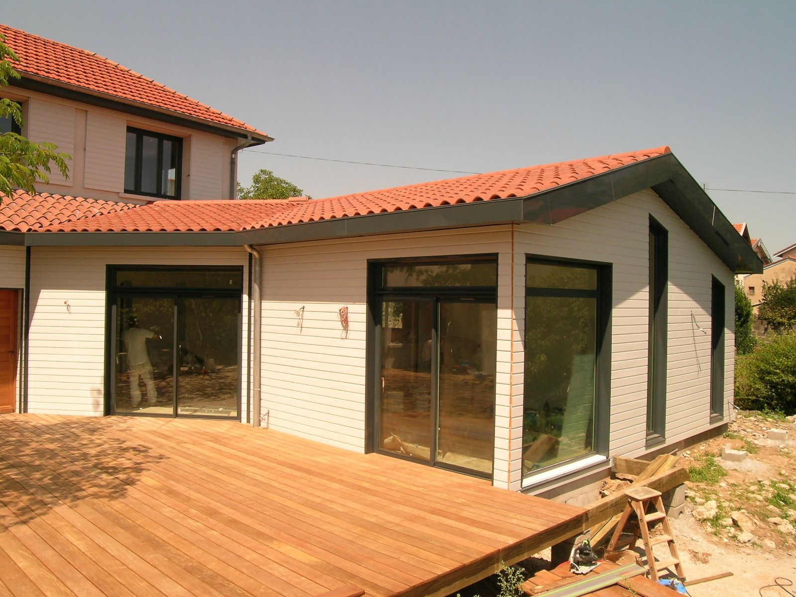 Terrasse arrière avec terrasse en bois, pergola, pelouse, ensemble de salle à manger et chaises longues.