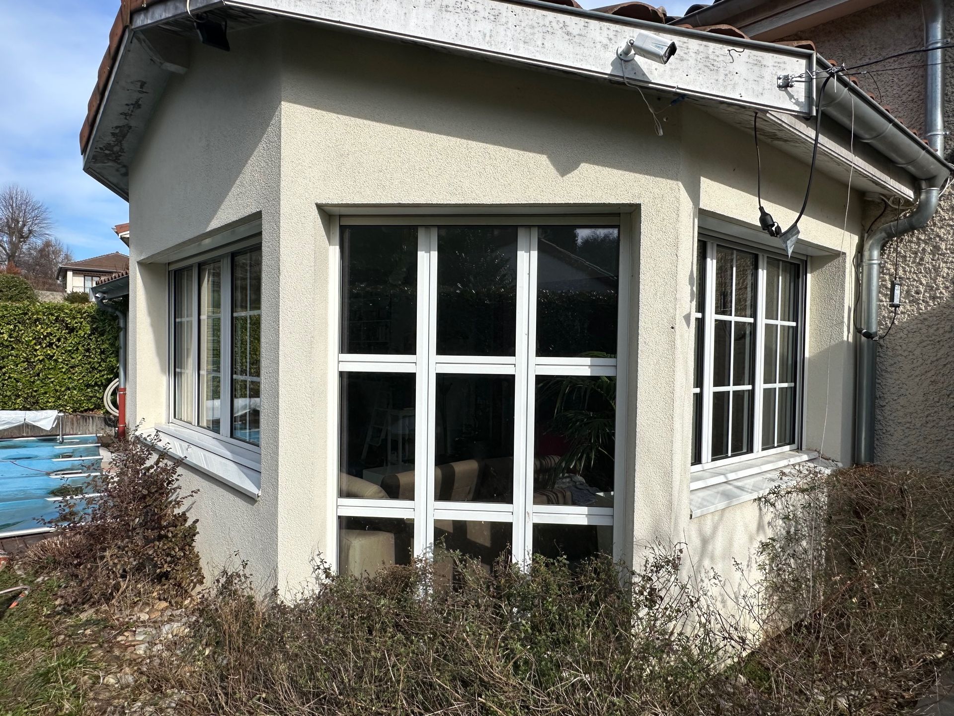 Extérieur d'un bâtiment aux multiples fenêtres à cadre blanc, entouré de végétation.