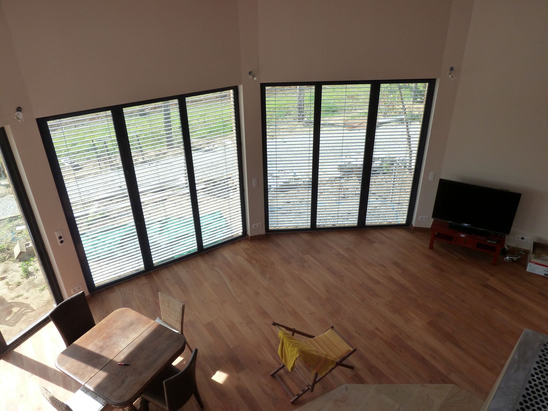 Vue en plongée d'une pièce avec de grandes fenêtres, un parquet et une table à manger.