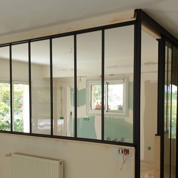 Intérieur avec cloison vitrée à cadre noir ; la lumière naturelle pénètre à travers, illuminant les murs bruts.