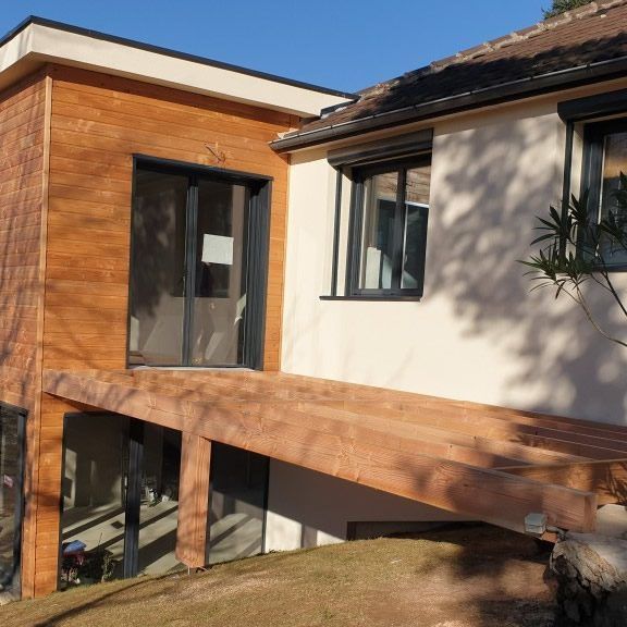 Maison moderne avec bardage en bois, terrasse et fenêtres par une journée ensoleillée.