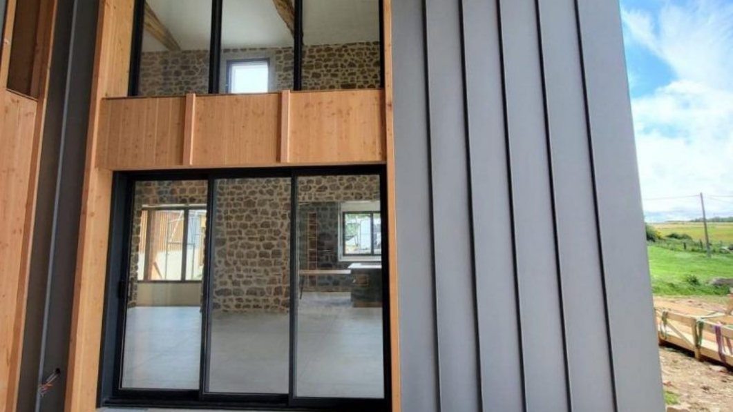 Façade de bâtiment moderne avec de grandes portes coulissantes en verre et un bardage vertical gris.