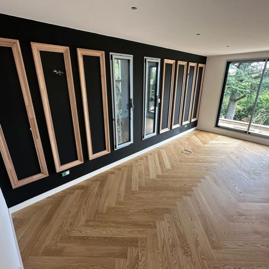 Pièce avec un mur noir, des cadres en bois, des fenêtres et un parquet en chevrons.